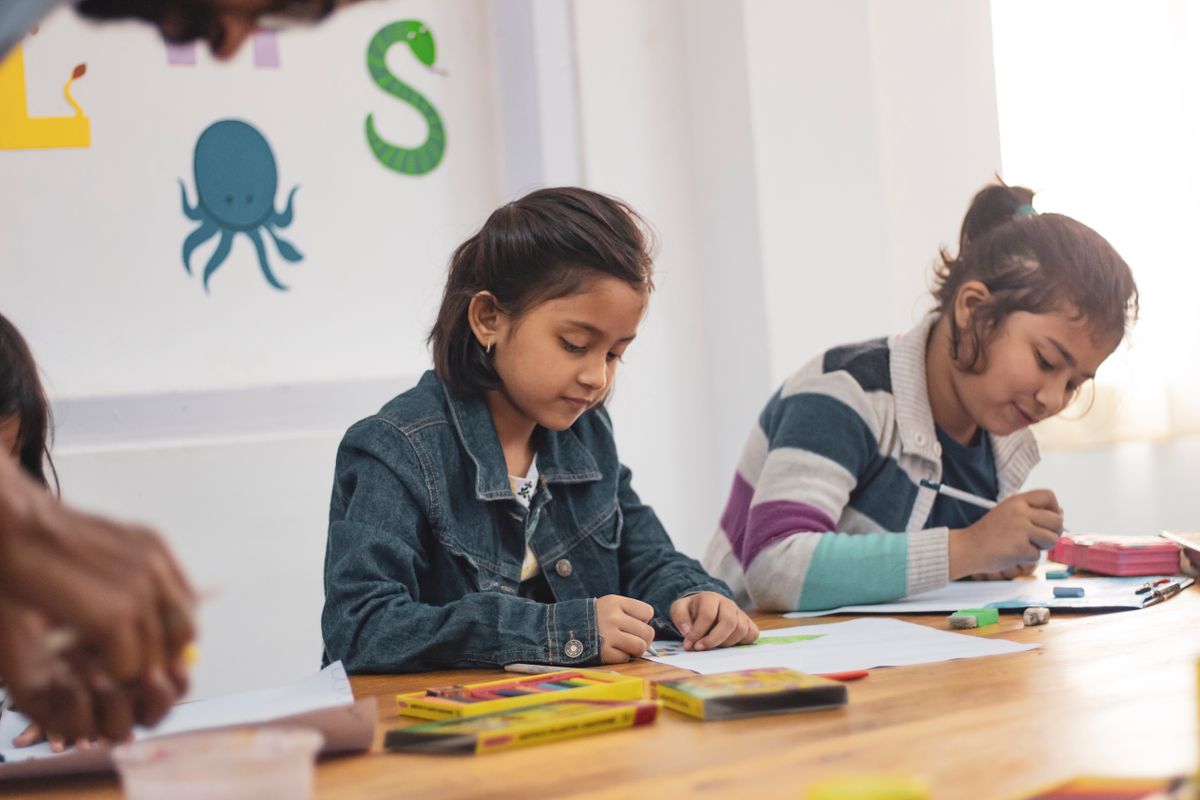 Two young girls drawing and colouring in class